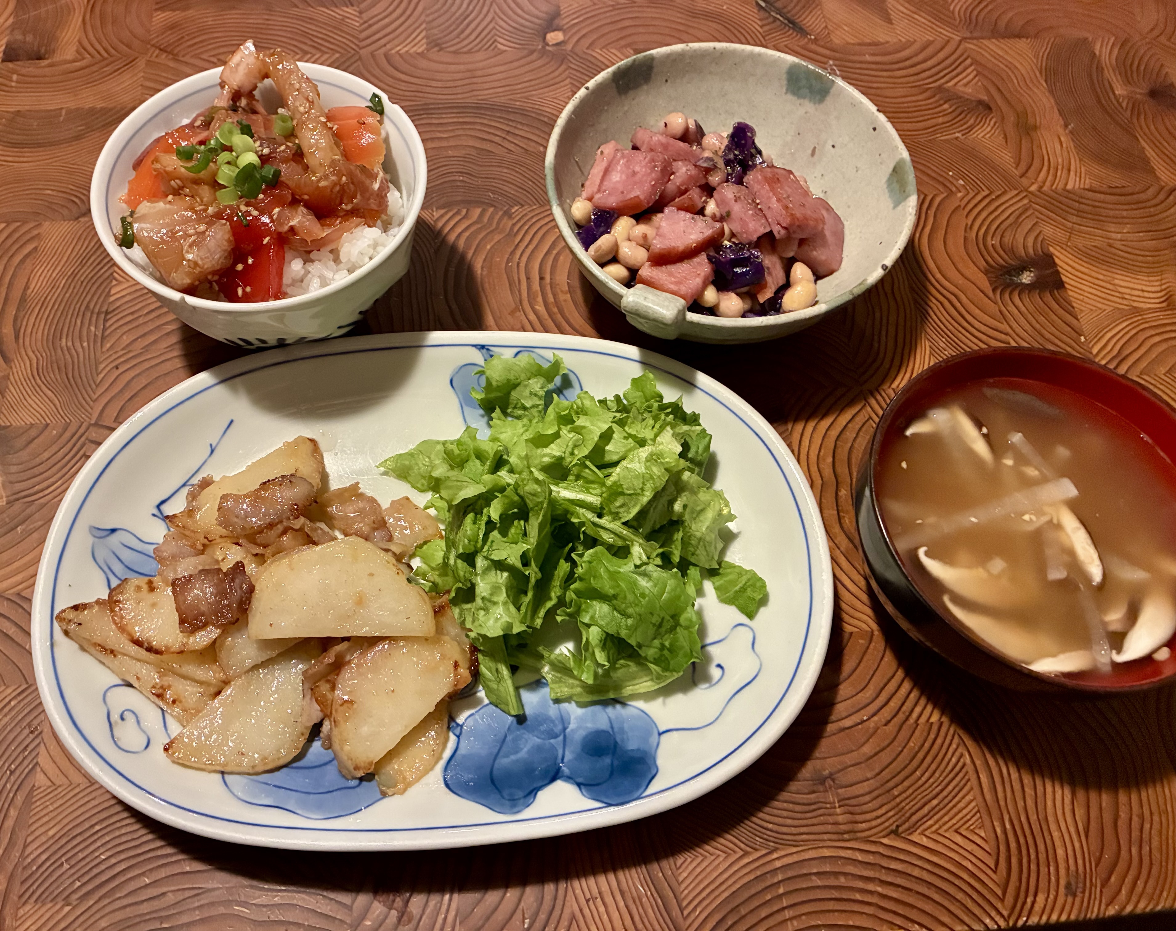 和洋折衷の料理が並んだ食卓。刺身の漬け丼、じゃがバター味噌炒め、紫キャベツの煮物、納豆汁が並んでいる。