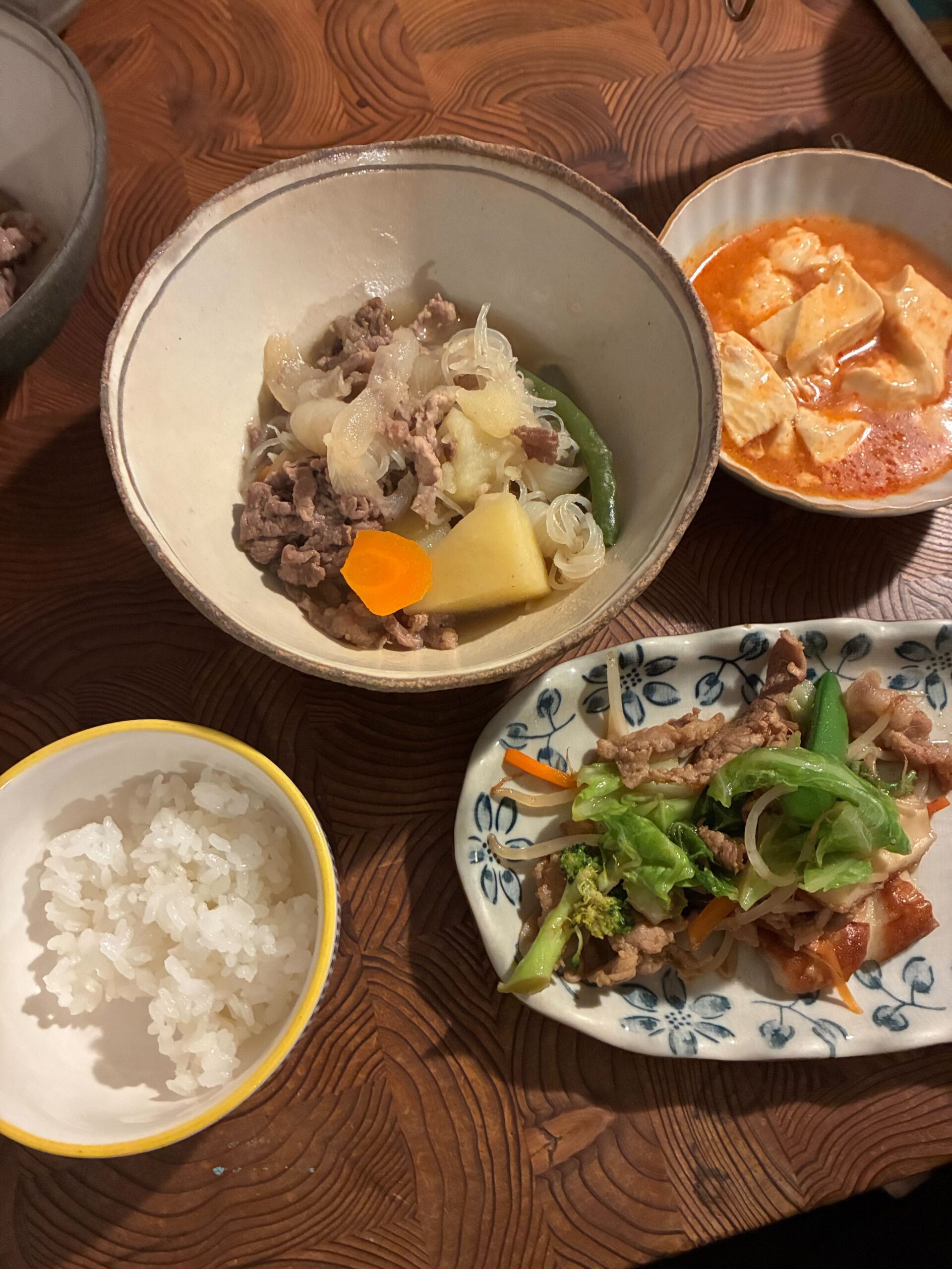 肉じゃがを中心に、麻婆豆腐、野菜炒め、白米が並ぶ家庭的な和食の食卓