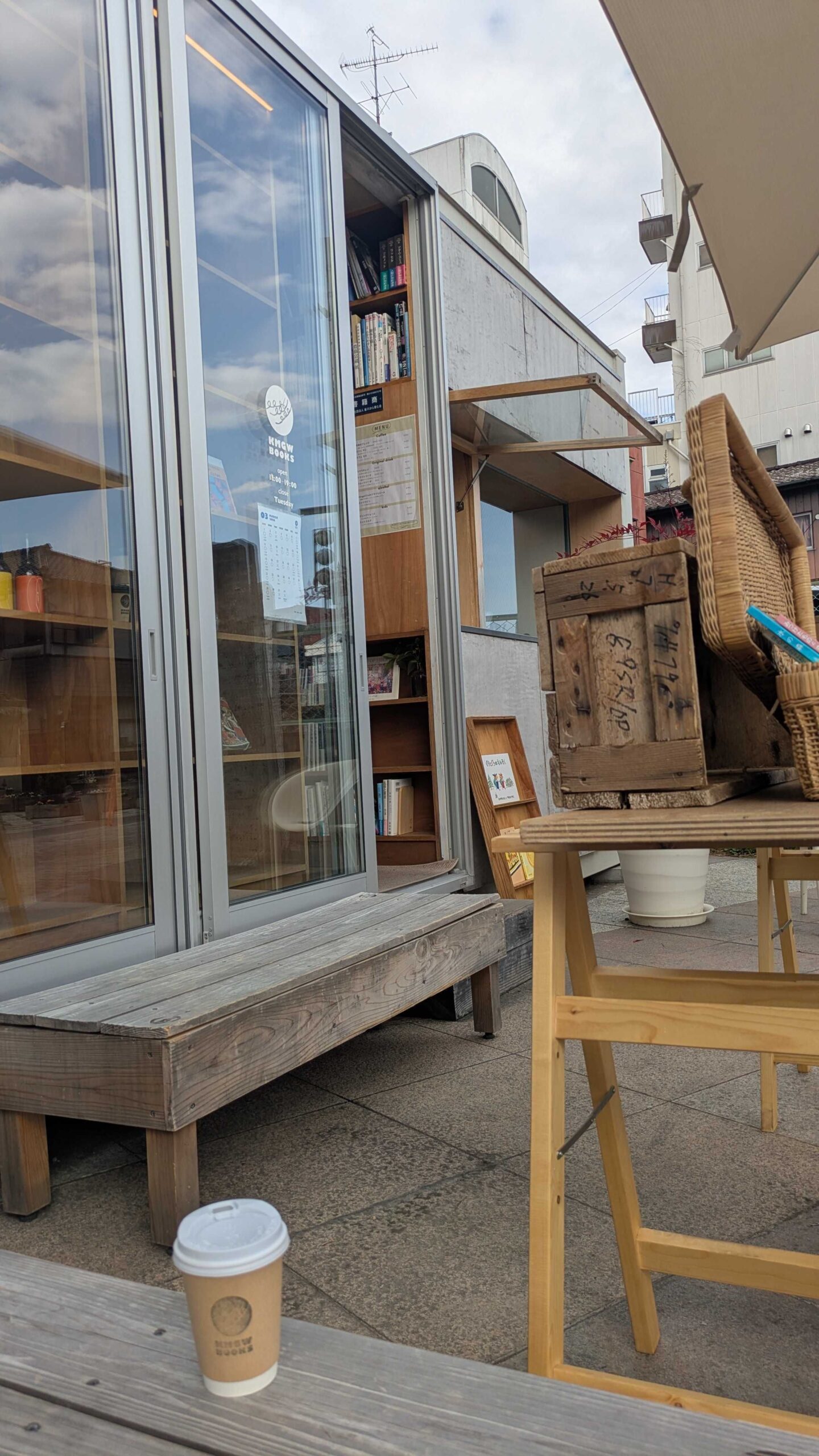 KMGW BOOKSの外にある木製のベンチとテーブル。テーブルの上にはテイクアウト用のコーヒーカップが置かれている。